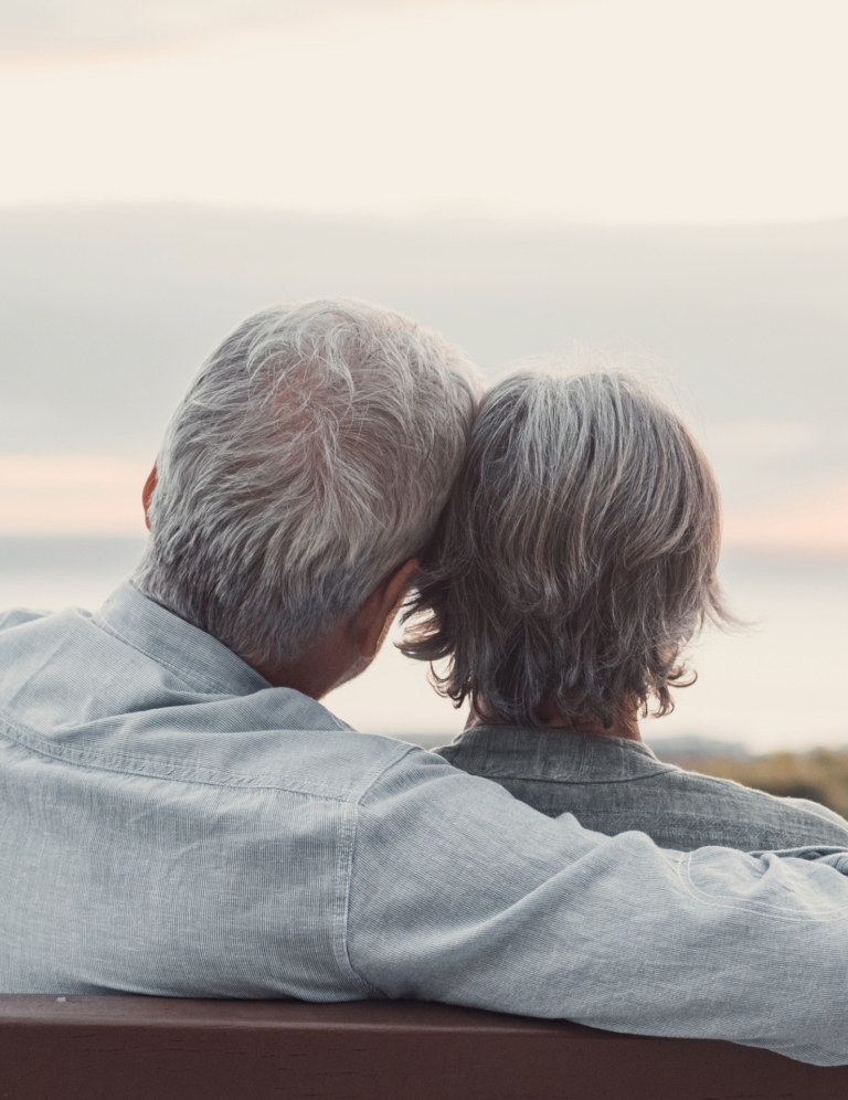 An older couple sits on a bench overlooking the ocean as they think about hiring estate planning attorneys.